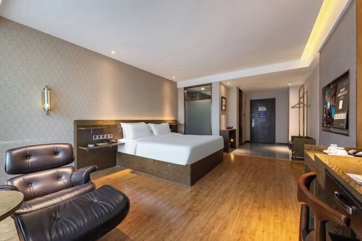 A modern hotel room with a large bed, a desk, a chair, and a small table.