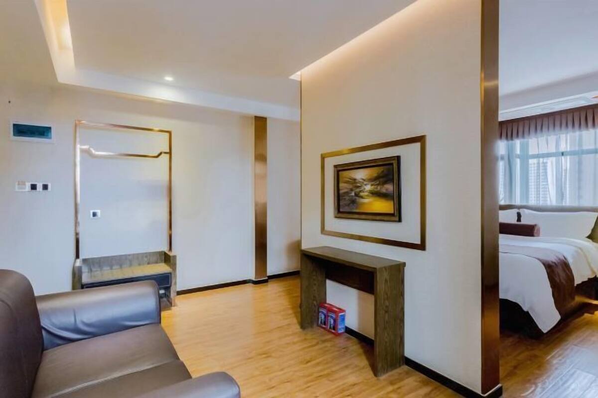 A hotel room with a bed, a seating area with a bench, a small table, and a wall-mounted picture.