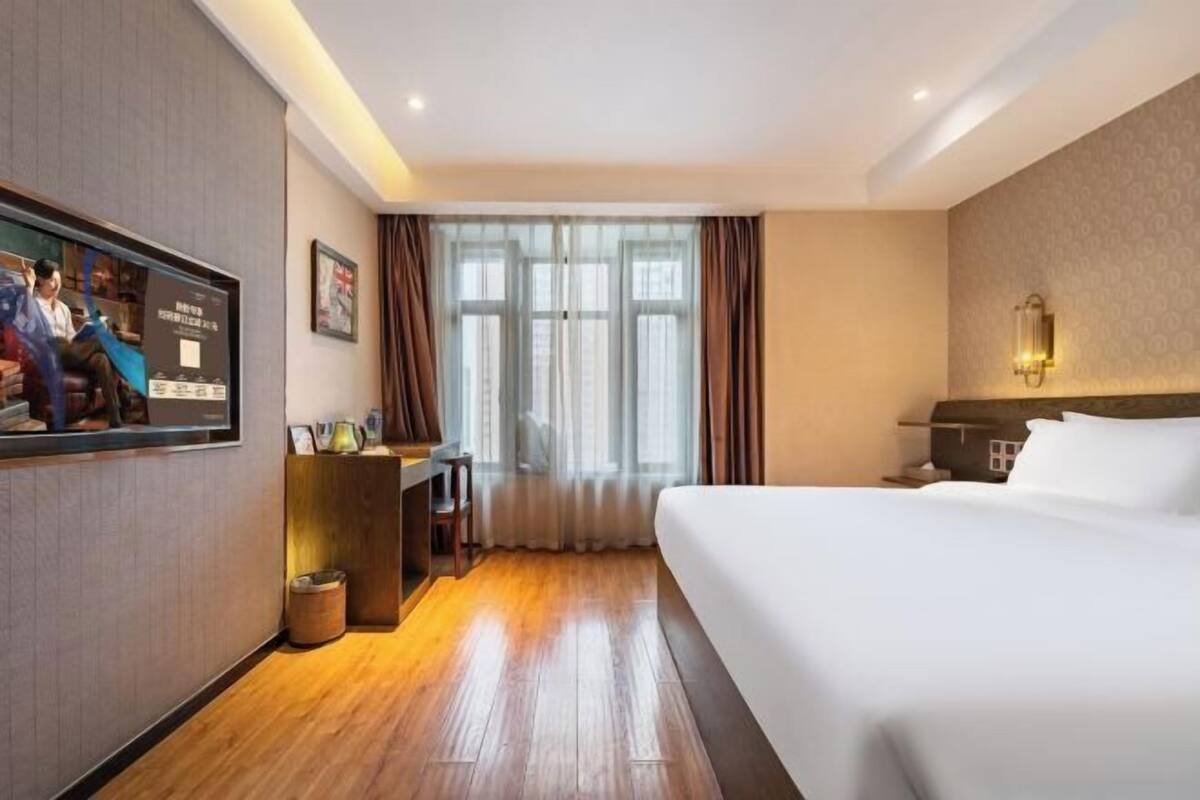 A hotel room with a large bed, a desk with a chair, a television, and a window with curtains.