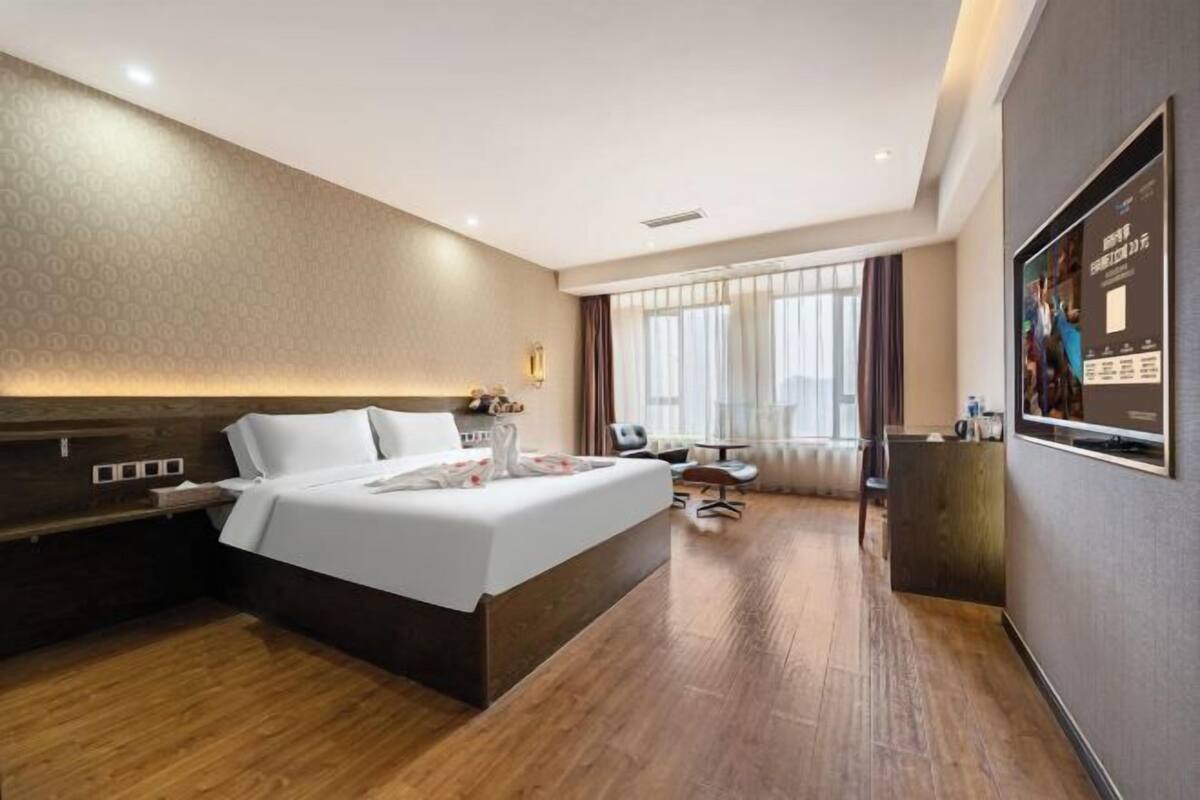 A hotel room with a large bed, a desk, a chair, a TV, and a window with curtains.