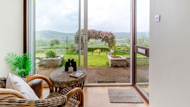 A balcony with a wicker table, chairs, and a view of a countryside landscape. - 3 bedroom accommodation in Membury (Membury)