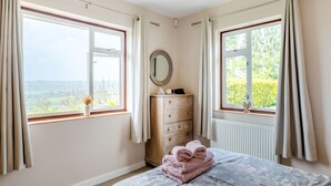 A bedroom with two windows, a dresser, a mirror, and a bed with a floral bedspread. - 3 bedroom accommodation in Membury (Membury)