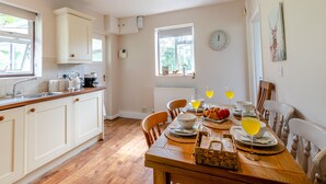 A well-lit kitchen with wooden cabinets, a dining table set with breakfast items, and a window providing natural light. - 3 bedroom accommodation in Membury (Membury)