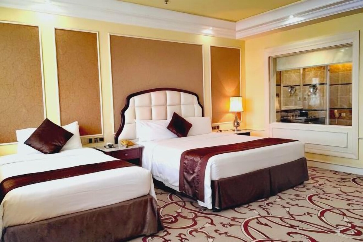 A hotel room with two beds, a large window, and a decorative mirror.