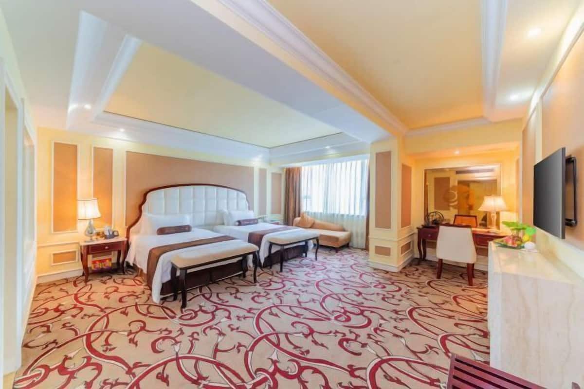 A hotel room with two beds, a sofa, a desk, and a television.