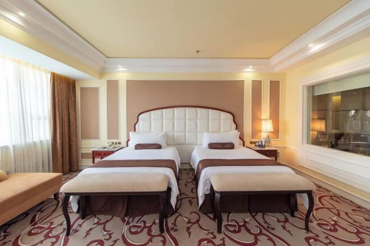 A hotel room with two beds, a sofa, a large window, and a patterned carpet.