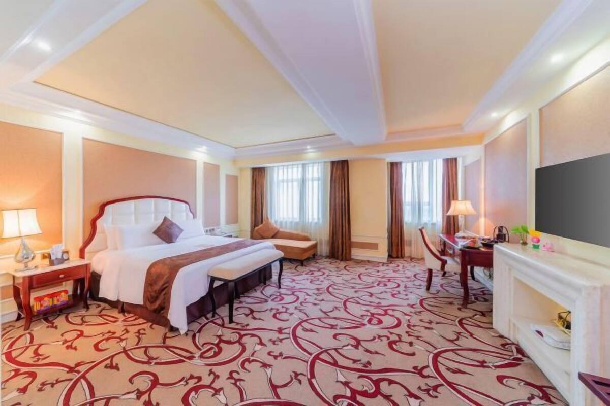 A hotel room with a bed, a desk, a chair, a fireplace, and a TV.