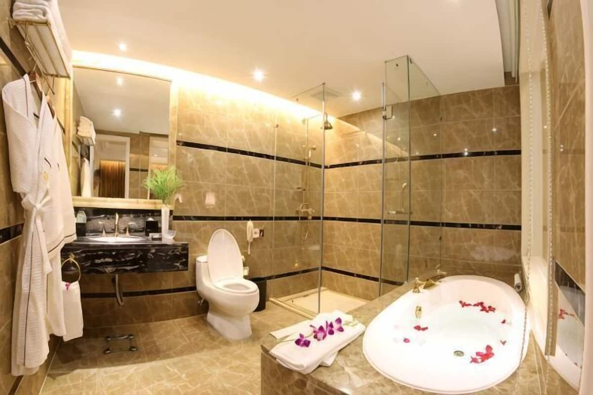 A modern bathroom with a glass-enclosed shower, a white bathtub with rose petals, a toilet, and a vanity with a mirror.