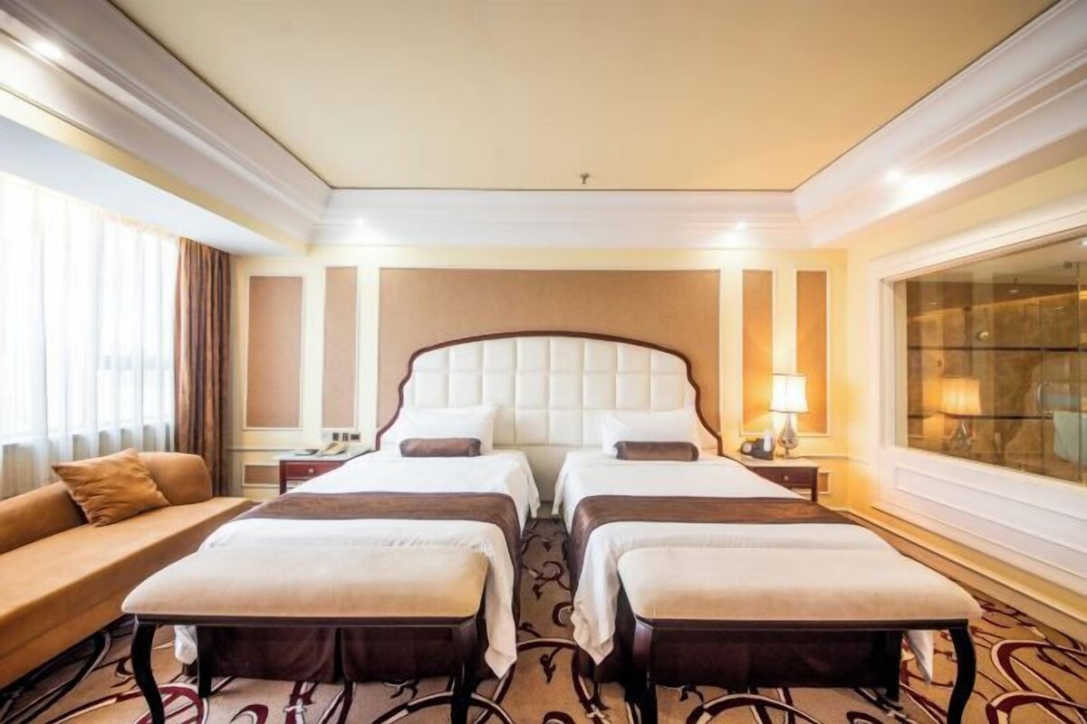A hotel room with two beds, a sofa, a desk, and a large window.