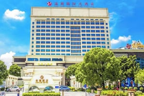 A multi-story hotel with a central entrance, surrounded by greenery and a parking area. - Jinxi International Hotel (Foshan)