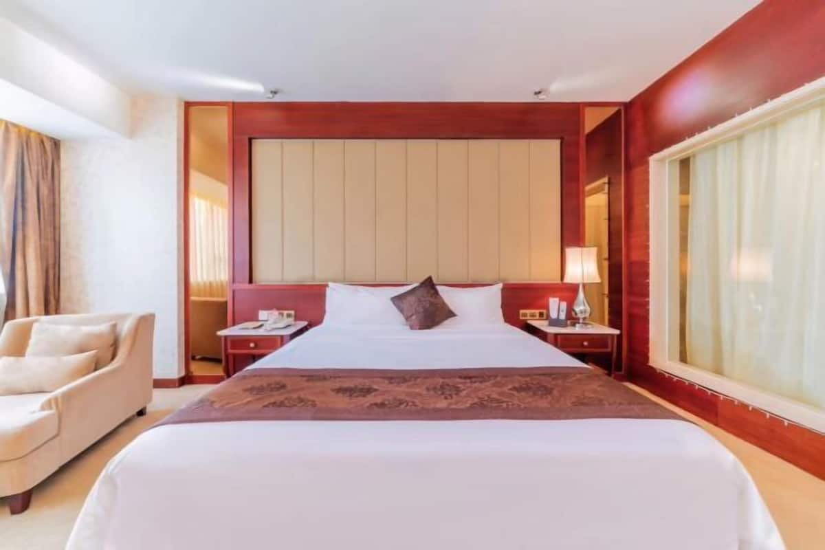 A hotel room with a large bed, a desk, a chair, and a window with curtains.
