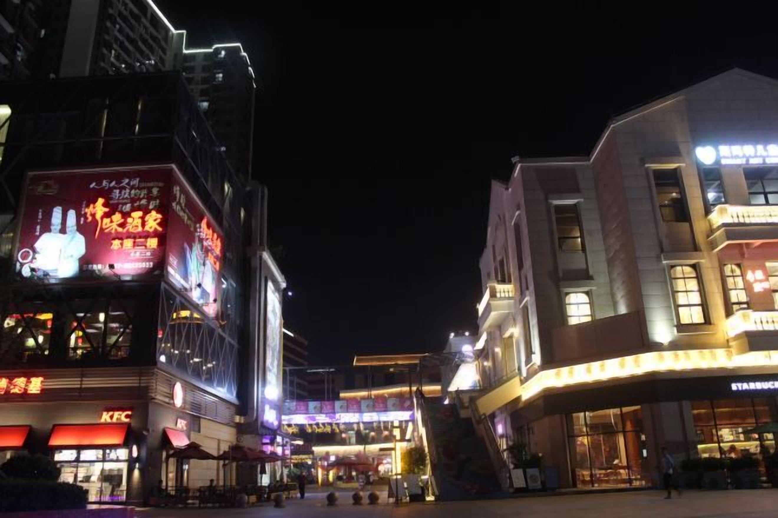 A nighttime urban street scene with commercial buildings, including a KFC and a Starbucks.