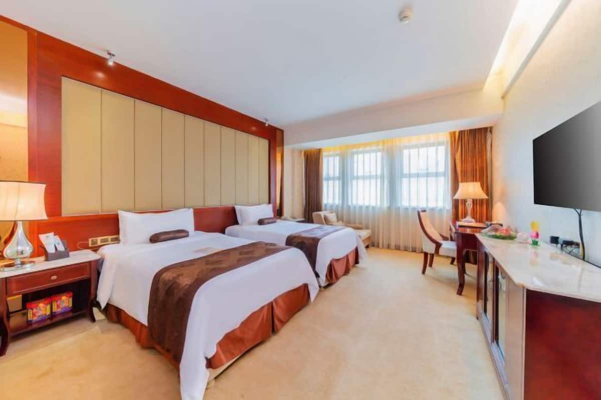 A hotel room with two beds, a desk, a chair, a TV, and a window with curtains.