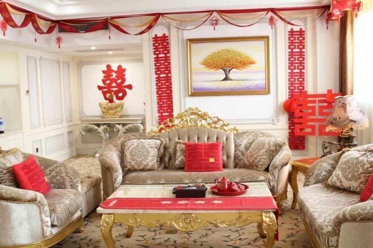 A traditional Chinese-style living room with ornate furniture, red decorations, and a painting of a tree.