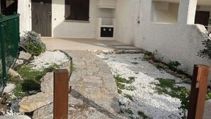 Un chemin de pierre mène à un bâtiment blanc doté d’un petit espace cuisine extérieur.