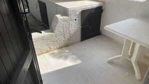 Un petit espace extérieur clos, avec une table blanche et une porte noire.