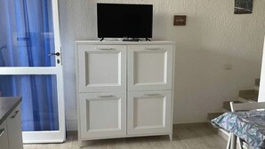 Une pièce avec un meuble blanc, un téléviseur posé dessus, un rideau bleu et une table recouverte d’une nappe à motifs.