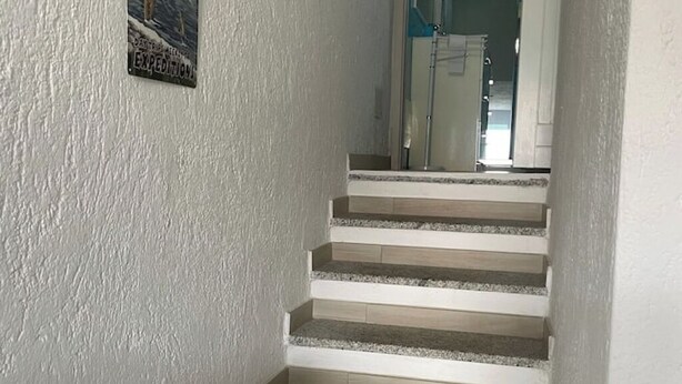 Un escalier aux murs blancs, avec une petite pancarte sur le côté gauche.