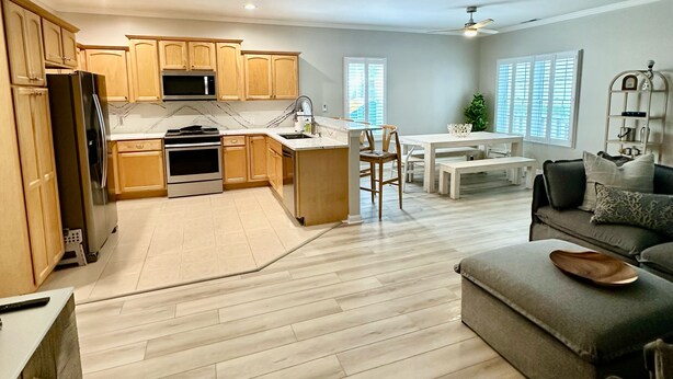 A modern kitchen with wooden cabinets, a refrigerator, and a microwave. There is a dining area with a white table and chairs. The living room has a grey sofa and a ceiling fan. - 4br/3ba + pool, close to beach. Pet friendly, WiFi, Parking, Quiet neighborhood (Rehoboth Beach)