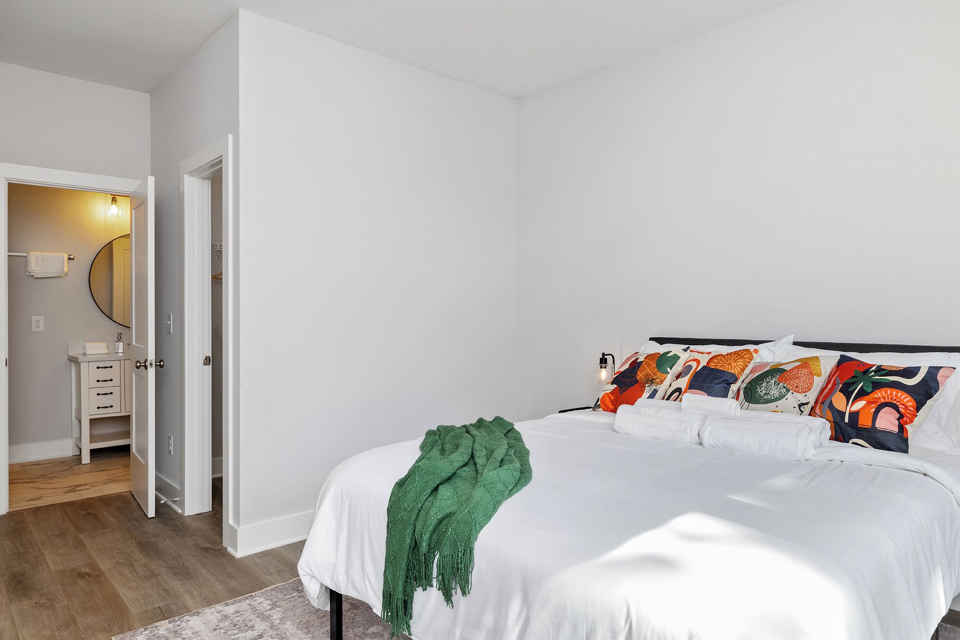 A bedroom with a bed, a green throw blanket, and colorful pillows.