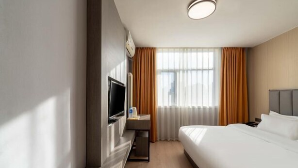 Ein Hotelzimmer mit einem Bett, einem Fernseher, einem kleinen Tisch und einem Fenster mit Vorhängen.