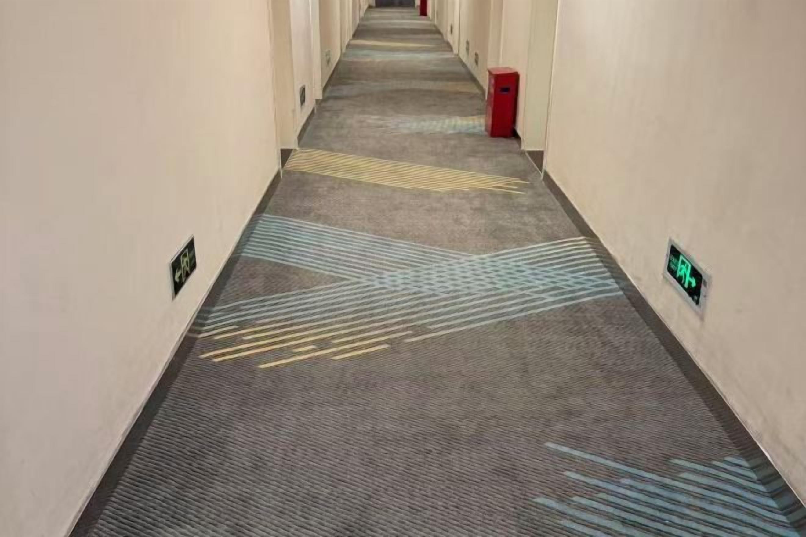 A hotel corridor with carpeted floors, directional arrows, and emergency exit signs.