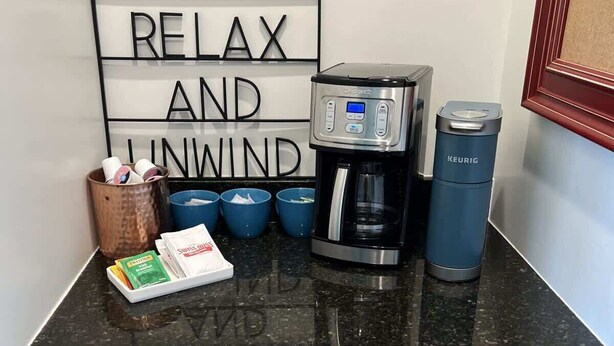 A kitchen counter with a coffee maker, a Keurig, and a sign that says 'RELAX AND UNWIND.' - Alum Ridge Retreat by Buffalo Mountain Getaway (Riner)