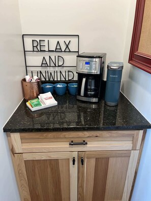 A kitchen counter with a coffee maker, a Keurig, and a sign that says 'RELAX AND UNWIND.' - Alum Ridge Retreat by Buffalo Mountain Getaway (Riner)