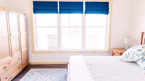 A bedroom with a bed, a window with blue curtains, a wooden wardrobe, and a small bedside table with a lamp. - Alum Ridge Retreat by Buffalo Mountain Getaway (Riner)