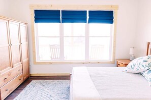 A bedroom with a bed, a window with blue curtains, a wooden wardrobe, and a small bedside table with a lamp. - Alum Ridge Retreat by Buffalo Mountain Getaway (Riner)