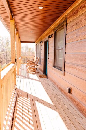 A wooden porch with a railing, a row of rocking chairs, and a door with a green frame. - Alum Ridge Retreat by Buffalo Mountain Getaway (Riner)