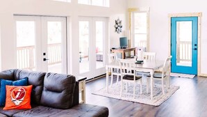 A spacious living area with a dark leather sofa, a dining table with chairs, and a blue door. - Alum Ridge Retreat by Buffalo Mountain Getaway (Riner)