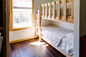 Ein Zimmer mit einem Etagenbett, einem Fenster mit Blick auf Bäume und Holzdielen.