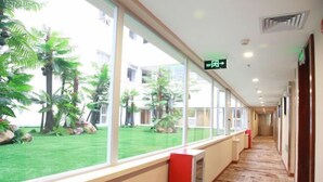 Un couloir d’hôtel avec de grandes fenêtres, une pelouse verdoyante et un mur d’accent rouge.