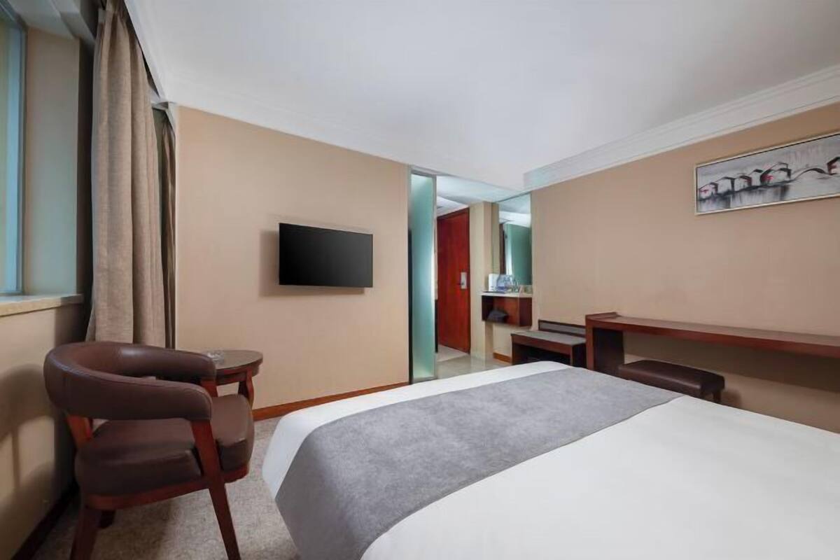 A hotel room with a bed, a desk, a chair, a television, and a painting on the wall.