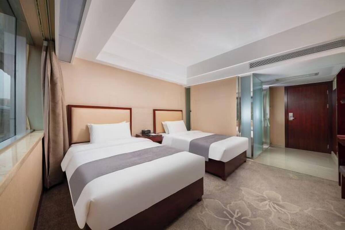 A hotel room with two beds, a window, a door, and a carpeted floor.
