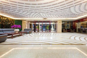 A hotel lobby with a modern design, featuring a seating area with sofas and a coffee table, a reception desk, and a patterned floor.