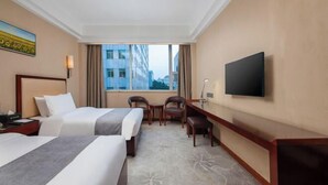 Une chambre d’hôtel avec deux lits, un bureau, une chaise, une télévision et une fenêtre donnant sur la ville.