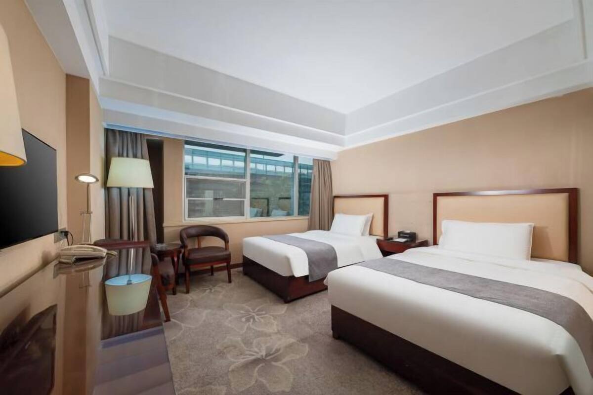 A hotel room with two beds, a desk, a chair, a TV, and a window with curtains.