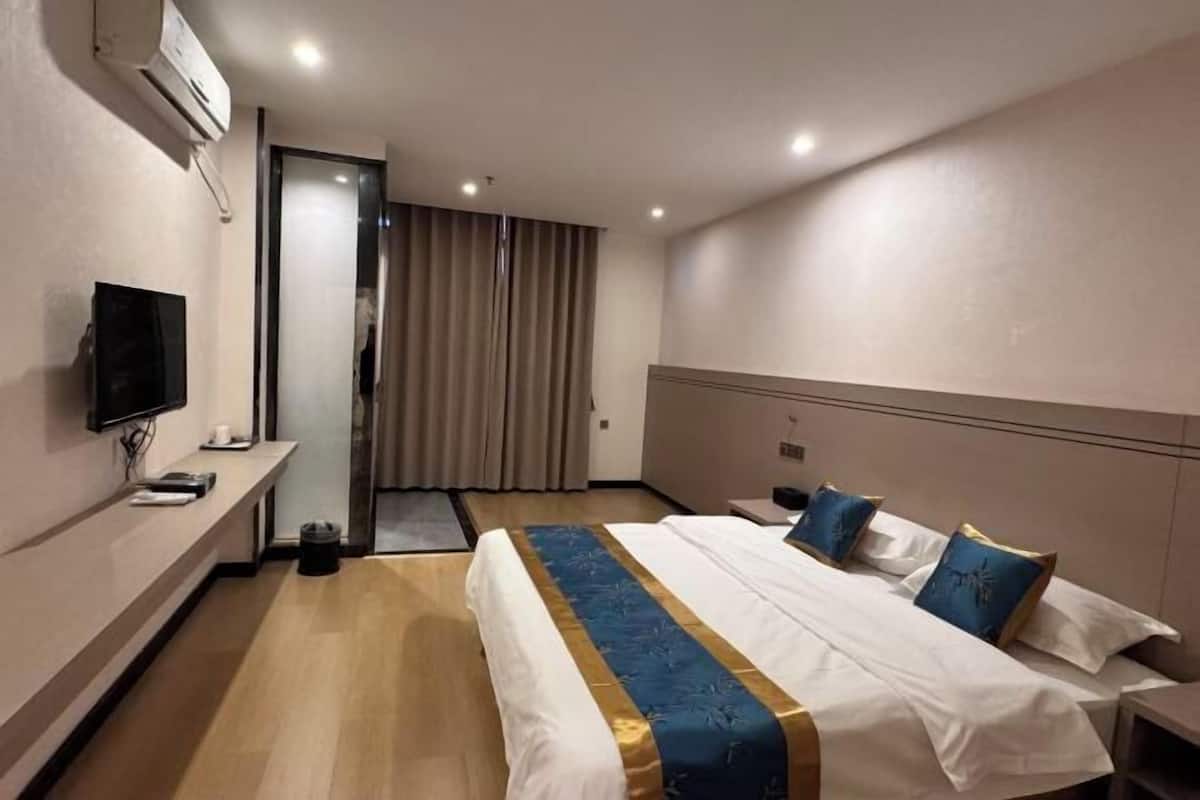 Una habitación de hotel con cama, televisor, escritorio y ventana con cortinas.