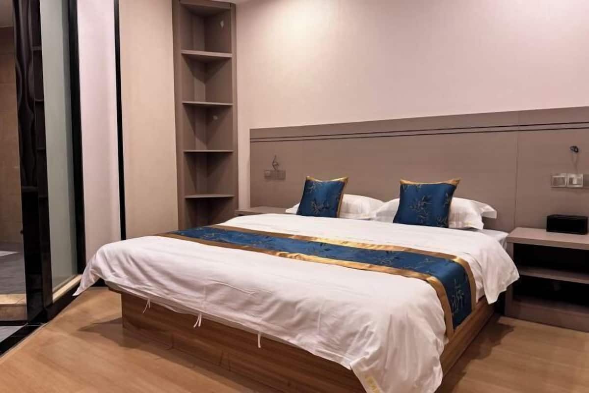 Una habitación de hotel moderna con una cama grande, una estantería empotrada y un ventanal de vidrio que da a un balcón.