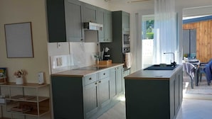 A modern kitchen with herringbone wood flooring, built-in green cabinets, and a central island with a sink.