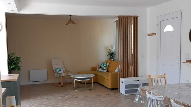 A spacious living area with a herringbone wooden floor, a round coffee table, a sofa, and a dining table with chairs.