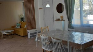 A dining area with a wooden table and chairs, a sofa, and a window with curtains.