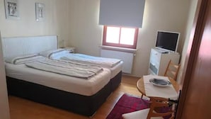 A small, well-lit bedroom with a bed, a desk with a chair, a radiator, and a window with blinds. - Vacation apartment no. 1, town center, Randersacker (Randersacker)