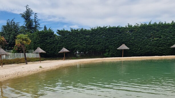 A sandy beach with a calm pool, surrounded by trees and thatched umbrellas. - Mobile home number 480 in camping 4☆ (Châteauneuf-de-Galaure)