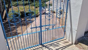 Une porte métallique bleue qui donne sur une cour bordée d’un mur de pierre et sur laquelle se trouve un bâtiment blanc.