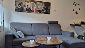 A living room with a grey sofa, two coffee tables, a colorful rug, a wall with a framed picture, and a wall decoration with the word "Espresso". - Vacation apartment "Amina" in Hahnenklee (Goslar)