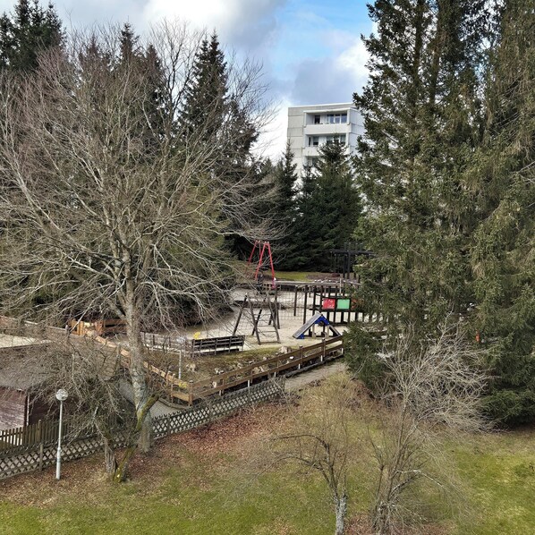 A park with playground equipment, a wooden fence, and a building in the background.