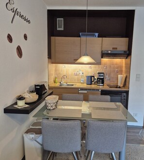A modern kitchen with a dining area, featuring a coffee machine, a kettle, and a sink.
